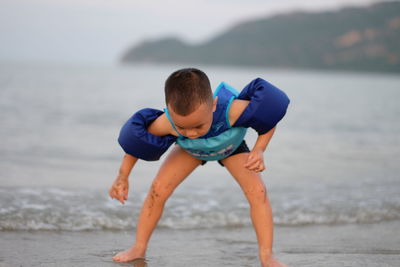 Boy wearing water wings while playing on shore at beach