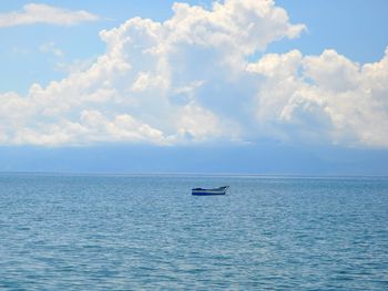 Boat sailing in calm sea against cloudy sky