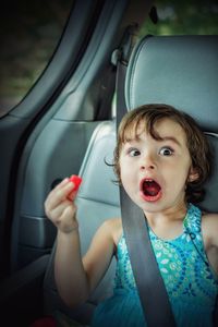 Portrait of cute girl making face while holding candy in car