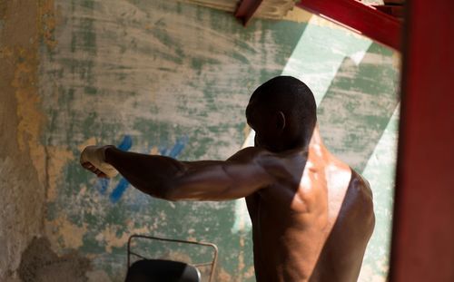 Rear view of shirtless man standing against window