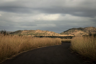 Road passing through field against cloudy sky