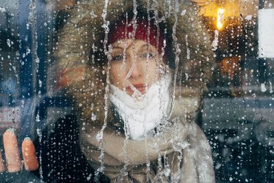 Portrait of woman looking through frozen window