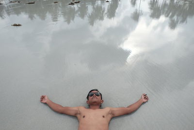 High angle view of man with arms outstretched lying on beach