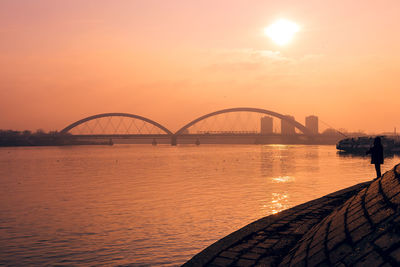 Silhouette bridge over river against sky during sunset