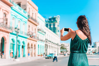 Woman photographing with mobile phone standing in city