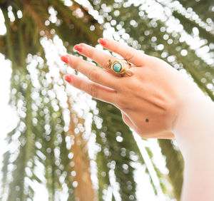 Cropped hand of woman showing ring against palm tree