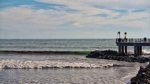 People on pier by sea against cloudy sky