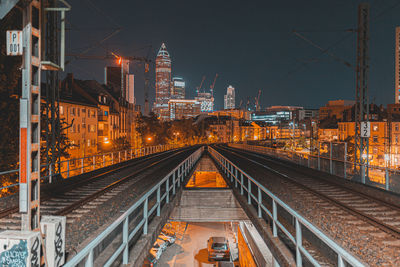 Illuminated railroad tracks amidst buildings in city at night