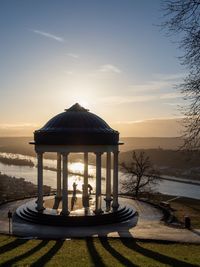 Gazebo by lake against sky during sunset