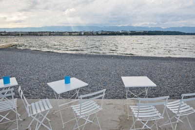 Empty chairs on beach against sky