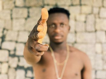 Portrait of shirtless man gesturing while standing against brick wall