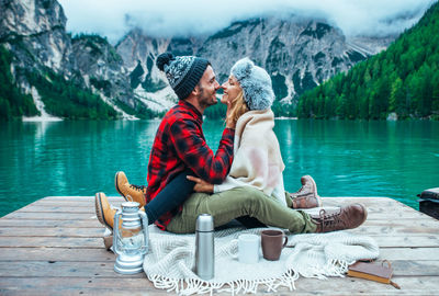 Friends sitting by lake against mountains