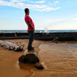 Full length of man on rock at beach against sky