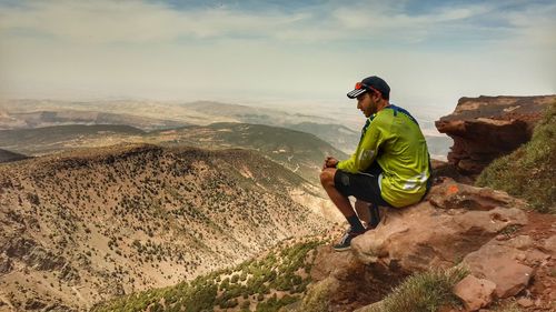 Full length of man sitting on mountain against sky