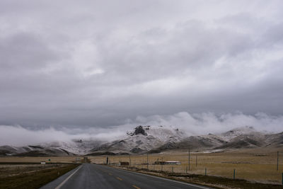 Road along landscape against cloudy sky