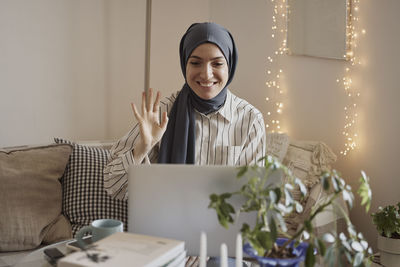 Happy female freelancer waving on video call over laptop while working at home