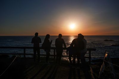 Silhouette people on beach against sunset sky