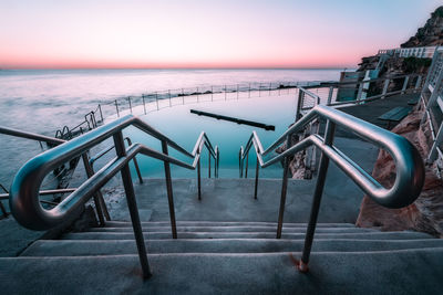 Metallic structure by swimming pool against sky during sunset