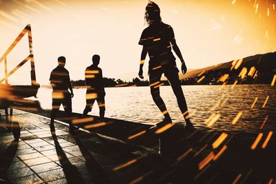 Silhouette people at promenade by lake against sky during sunset