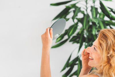 Low angle view of young woman holding plant against white background