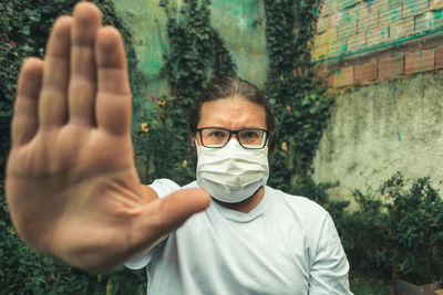 Portrait of man wearing flu mask gesturing stop outdoors