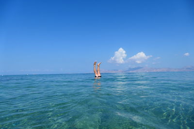 Man swimming in sea against clear blue sky in handstand