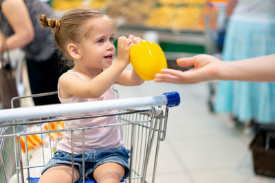 Cute girl receiving yellow bell pepper at supermarket