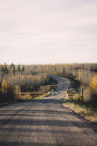 Country road amidst trees against sky