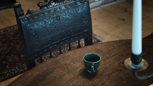 Close up view of artisanal tea cup on wooden table with old vintage wood royal armchair 
