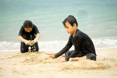 Siblings playing with sand at beach