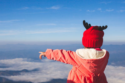 Girl in warm clothing pointing against blue sky during winter