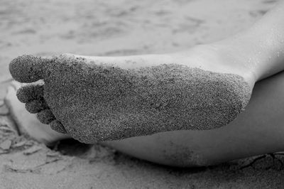 Low section of woman with sand on foot lying at beach