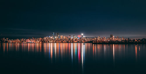 Illuminated buildings by river against sky at night