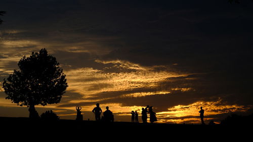 Silhouette people standing on field against cloudy sky during sunset
