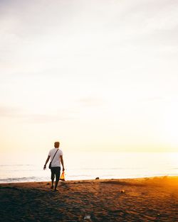 Man standing on beach against sky during sunset