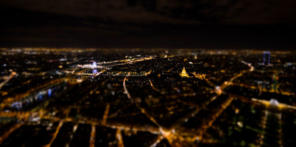 Tilt-shift image of illuminated cityscape against sky at night