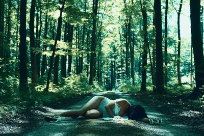 Full length of seductive woman lying amidst trees on road in forest