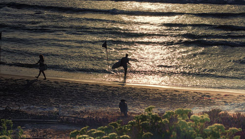 Silhouette people standing on beach against sky during sunset