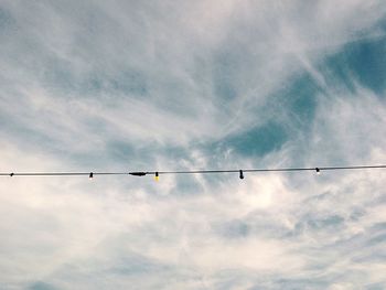 Low angle view of birds perching on cable against sky