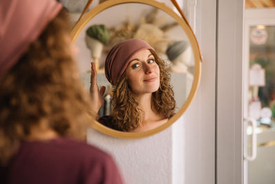 Smiling fashion designer fixes her headband while admiring her reflection in a round mirror