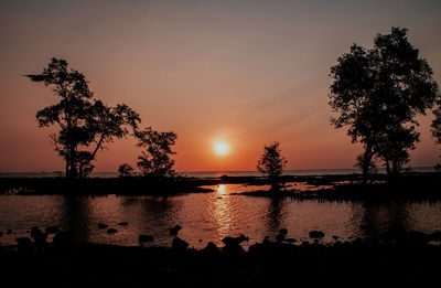 Silhouette trees by lake against sky during sunset