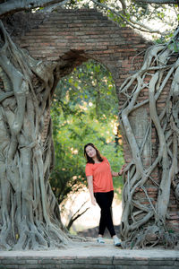 Full length of woman standing by tree trunk