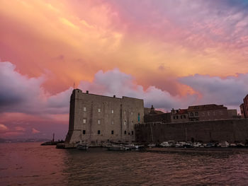 Buildings by sea against sky during sunset
