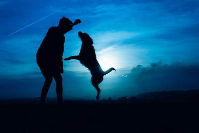 Silhouette of a young man with his dog jumping with blue night light