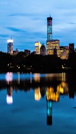 Illuminated buildings by river against sky