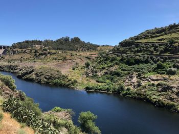 Scenic view of river by mountains against clear blue sky