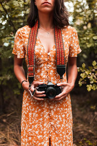Midsection of woman holding camera standing in forest