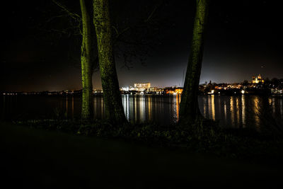 Illuminated city by river against sky at night