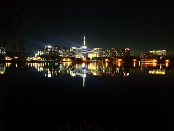 Illuminated city by sea against clear sky at night