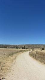 Road by landscape against clear blue sky